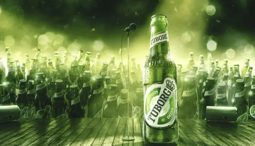 Zielona butelka piwa Tuborg Green na scenie, otoczona tłumem innych butelek. W tle mikrofon.