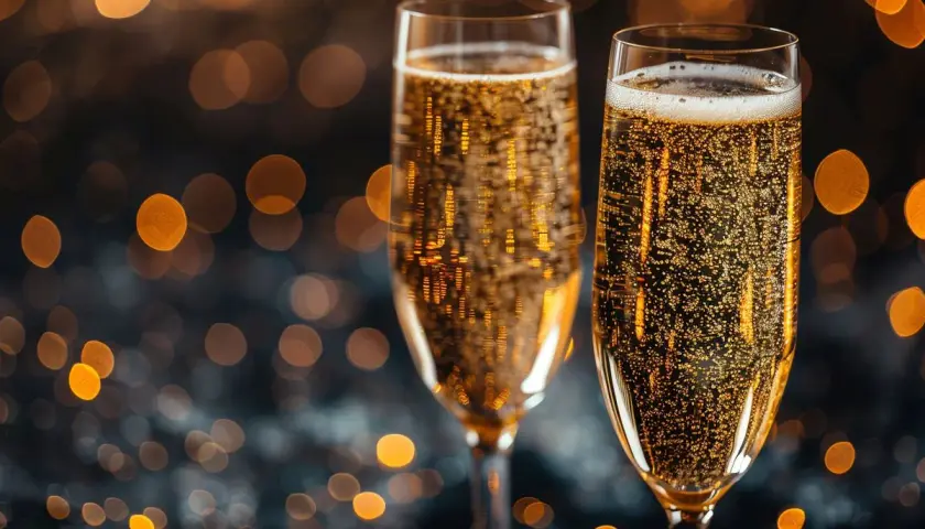 Dwa kieliszki musującego prosecco, które często mylone jest z szampanem, na tle rozmytych, złotych świateł.