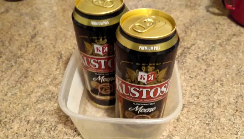 Dwa puszki piwa Kustosz Premium Pils w plastikowym pojemniku. Idealne na wieczór z dobrym **kustosz piwo**.