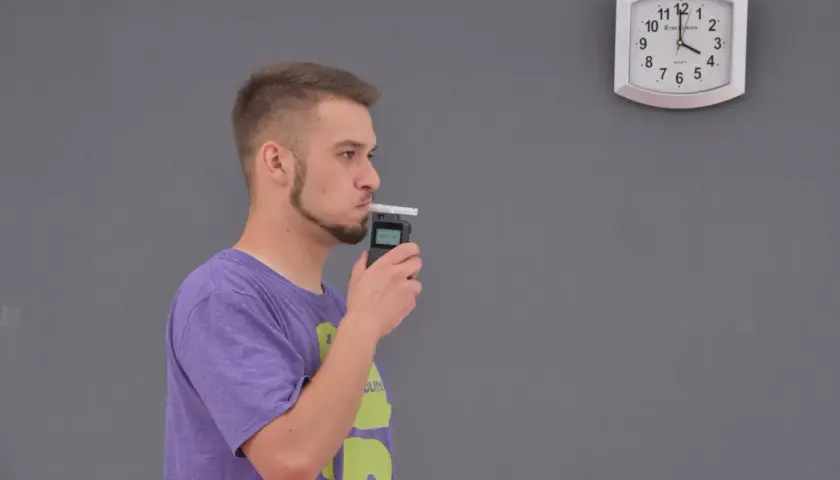 Mężczyzna dmucha w alkomat, obok wisi zegar.