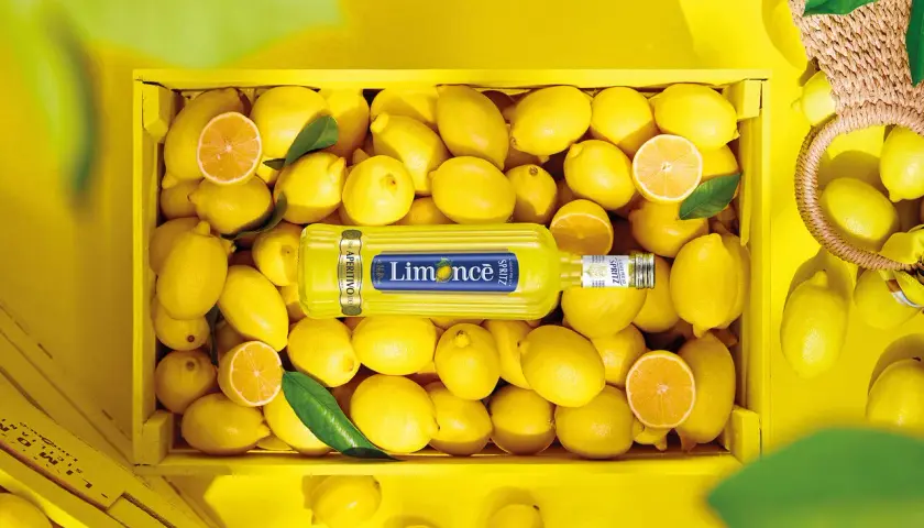 Butelka Limoncé Spritz leżąca w skrzynce pełnej cytryn.