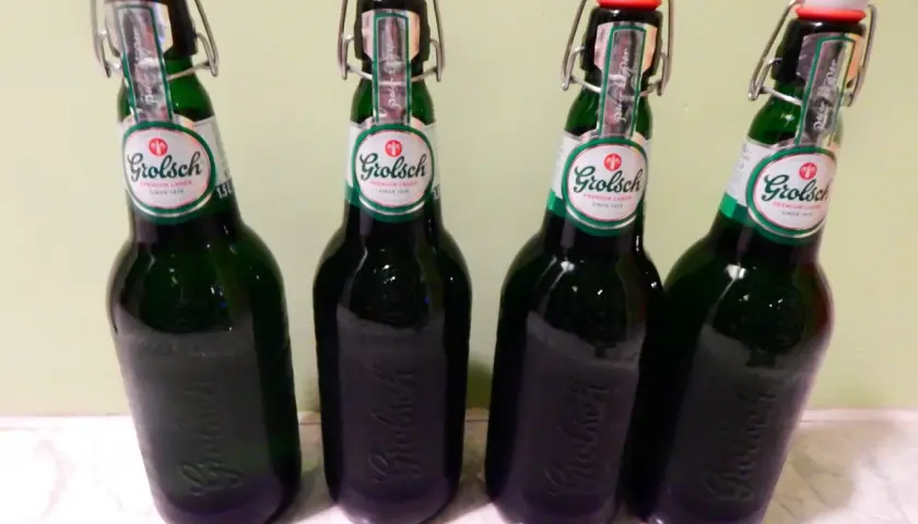 Cztery butelki piwa Grolsch z charakterystycznymi zamknięciami typu swing-top, stojące obok siebie.