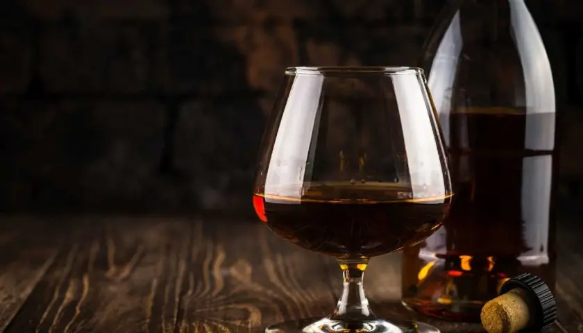 Kieliszek z bursztynowym brandy Stock 84 i butelka na drewnianym stole.