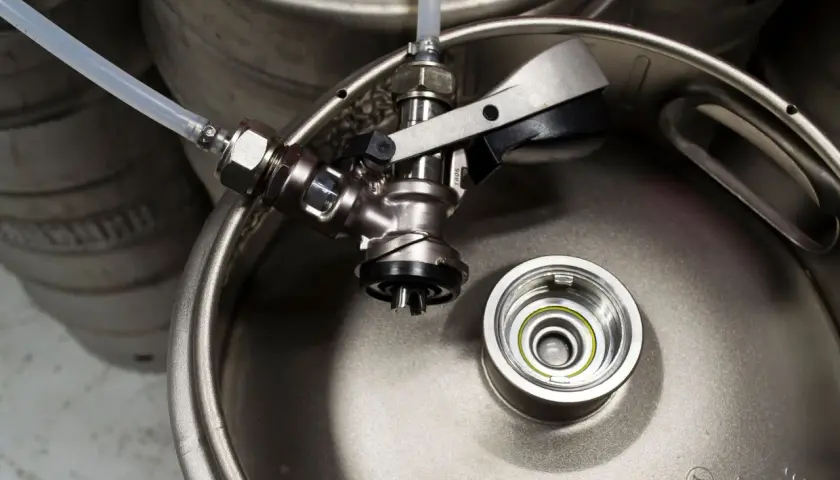 Metalowy keg piwa z podłączonym kranikiem i wężykiem. Gotowy do nalewania orzeźwiającego trunku.