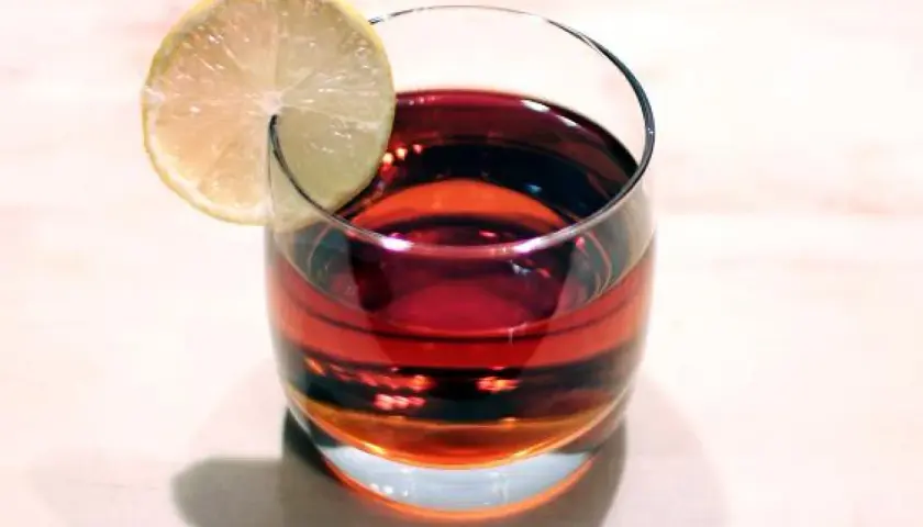 Szklanka z ciemnoczerwonym Martini Rosso, ozdobiona plasterkiem cytryny, stoi na jasnym blacie.