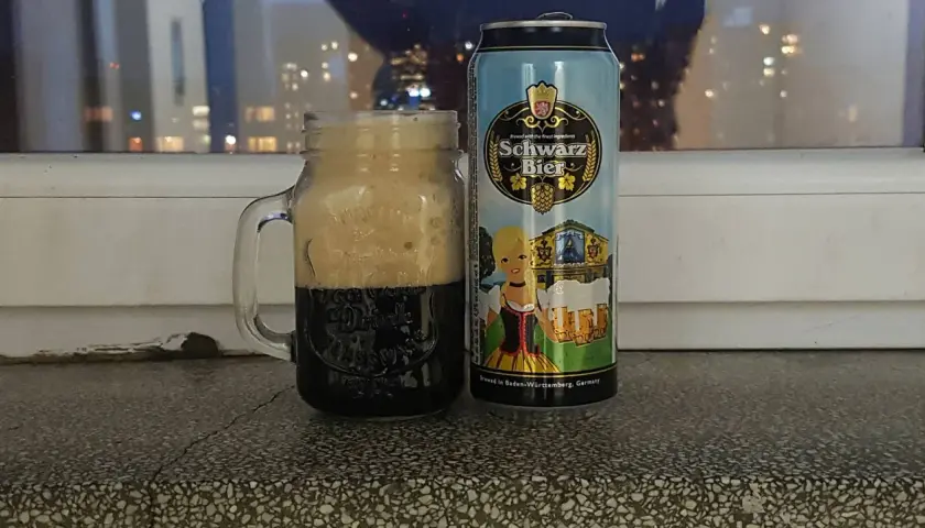 Perlenbacher Schwarz Bier w kuflu, obok puszka piwa. W tle nocne światła miasta.