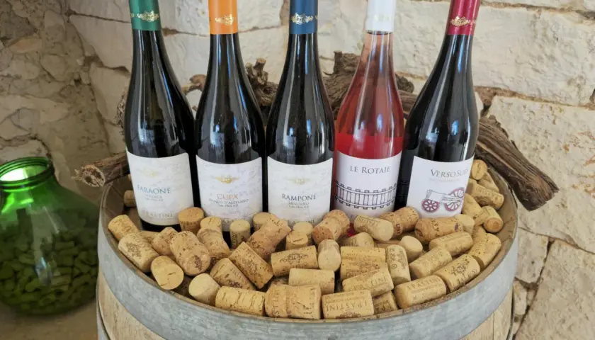 Pięć butelek wina, w tym różowe, na beczce pełnej korków. Idealne na tanie wino i wieczorne degustacje.