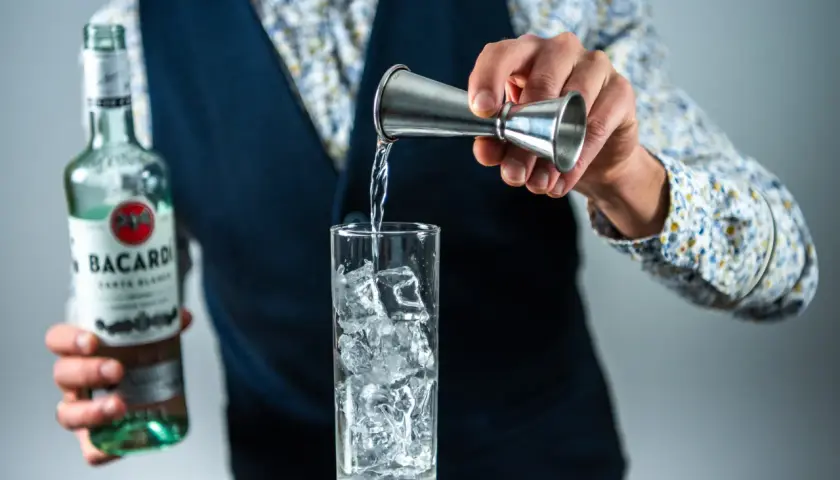 Barman nalewa rum z butelki Bacardi do szklanki z lodem, przygotowując drinka rum z colą.