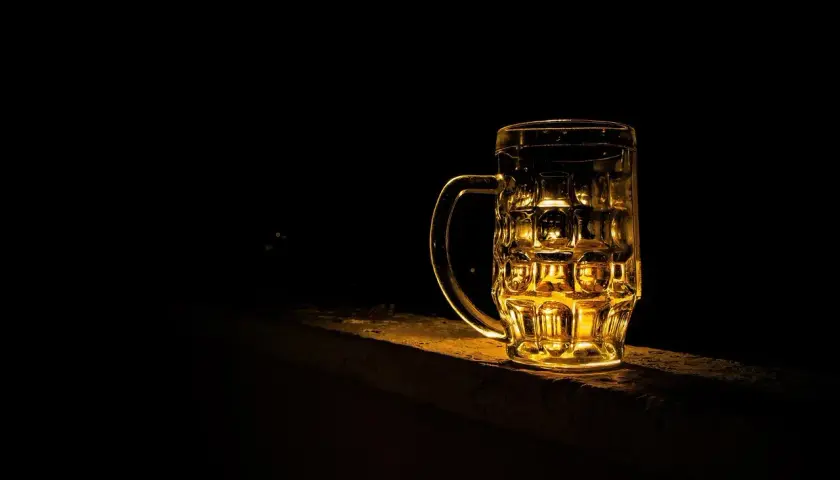 Złocisty kufel piwa Grimbergen, podświetlony od tyłu, stoi na kamiennym murku w ciemności.