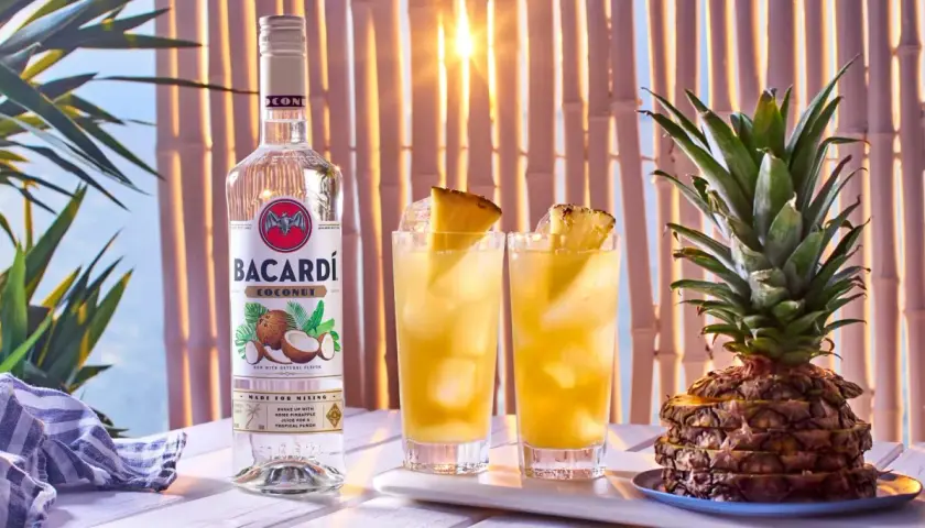Butelka Bacardi Coconut obok dwóch drinków z ananasem i cała ananasowa piramidka. Idealne na tropikalne przyjęcie!