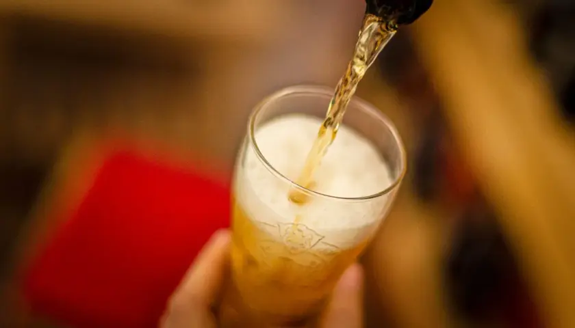 Z butelki leje się złociste piwo Peroni do szklanki, tworząc obfitą pianę.