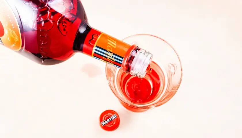 Czerwony Martini Fiero nalewany do kieliszka. Obok leży czerwona zakrętka z logo Martini.