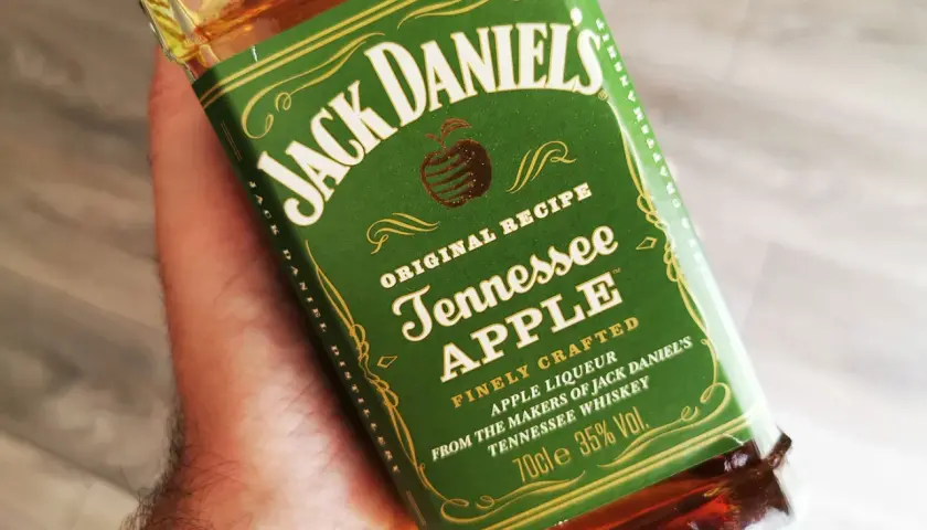 Dłoń trzyma butelkę Jack Daniel's Tennessee Apple. Ten miodowy likier jabłkowy to idealny dodatek do wieczoru.