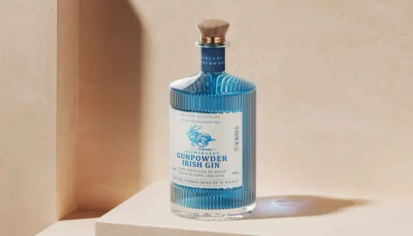 Niebieska butelka ginu Drumshanbo Gunpowder Irish Gin, inspirowanego podróżami do Bombaju, z drewnianym korkiem i etykietą z jeleniem.