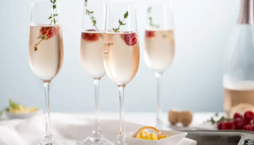 Cztery kieliszki orzeźwiającego prosecco rose z malinami i gałązkami tymianku, gotowe na toast.