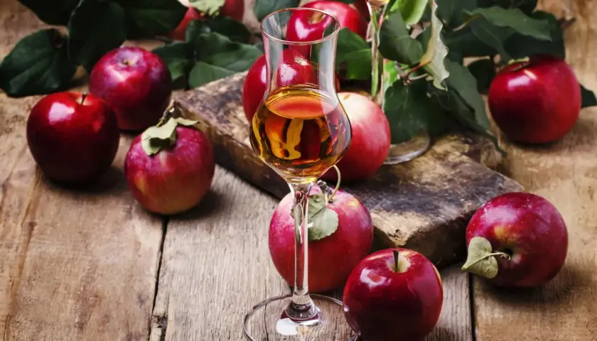 Czerwone jabłka i kieliszek z bursztynowym płynem. To właśnie calvados, destylat z jabłek, który zachwyca smakiem.