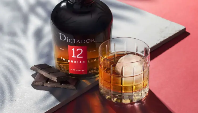 Butelka rumu Dictador 12 Years Colombian Rum obok szklanki z drinkiem i kawałków czekolady.