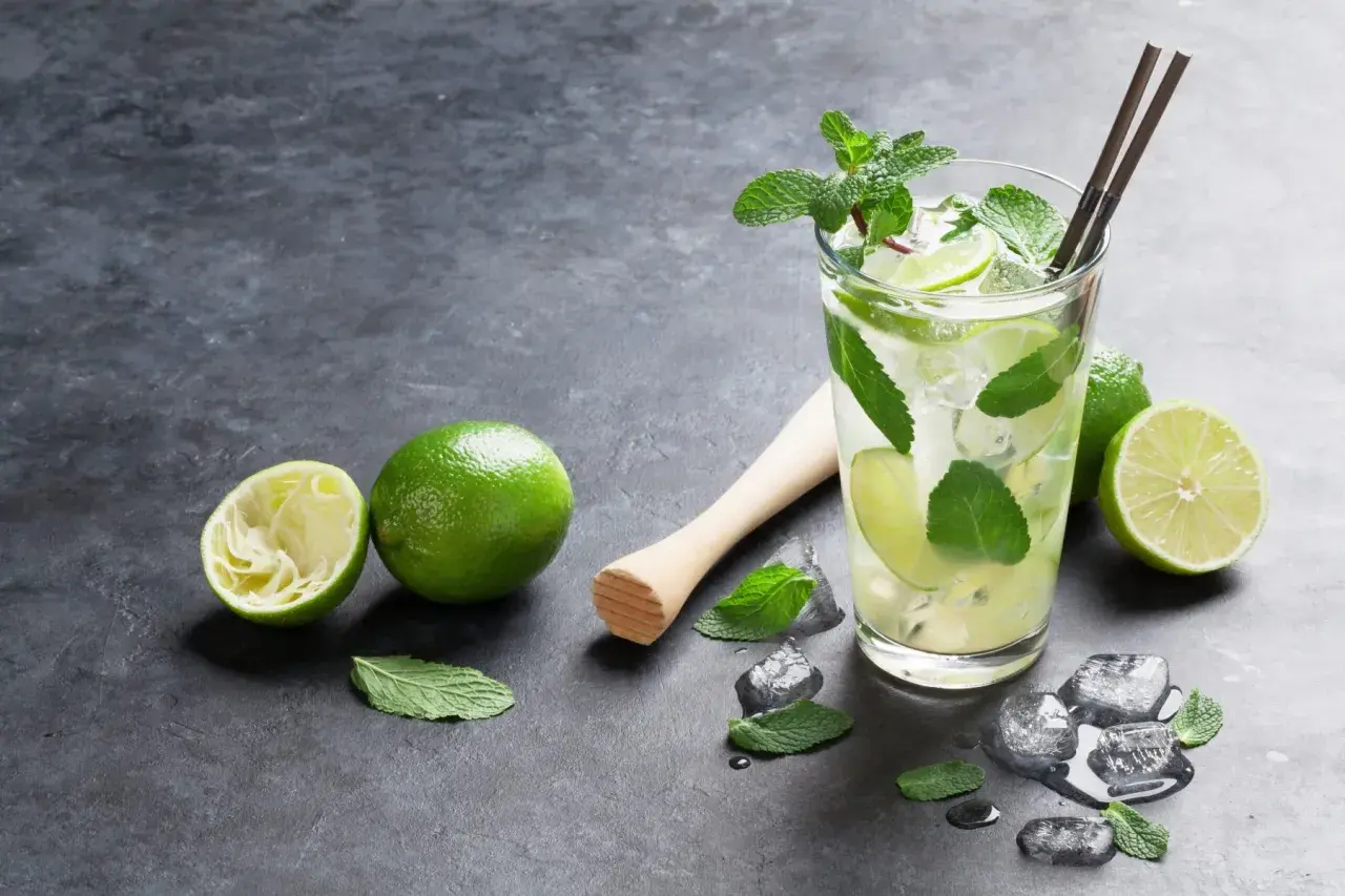 Orzeźwiający **mojito** z limonką i miętą, obok świeże limonki i kostki lodu.