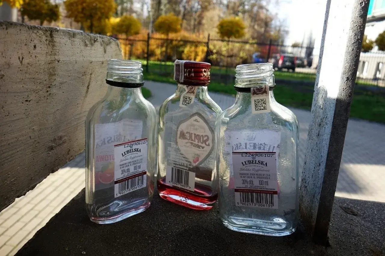 Trzy puste butelki po alkoholu, w tym jedna z czerwonym płynem, leżą na betonowym murku. Małpka alkoholowa, symbol beztroski, ale i problemu.