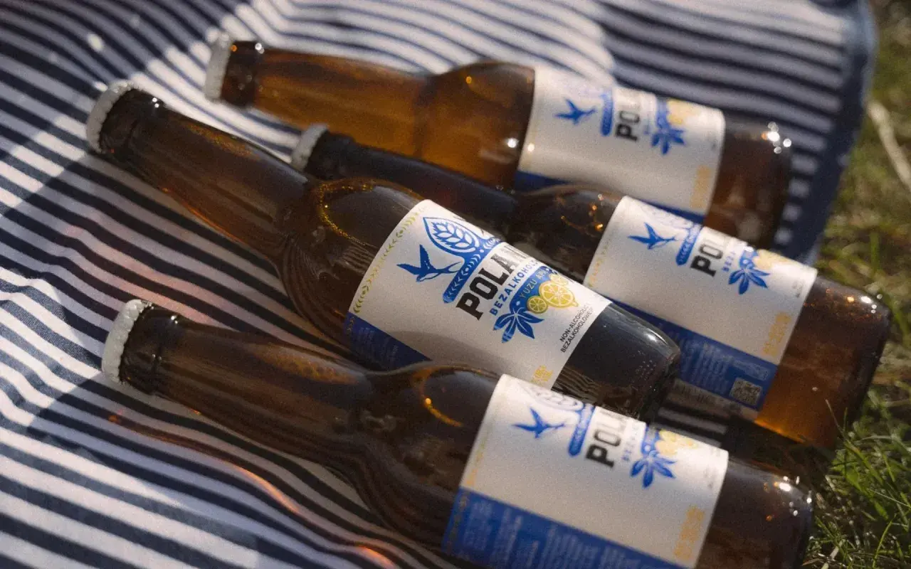 Kilka butelek piwa 0% na kocu w paski. Orzeźwiający napój na letni dzień.
