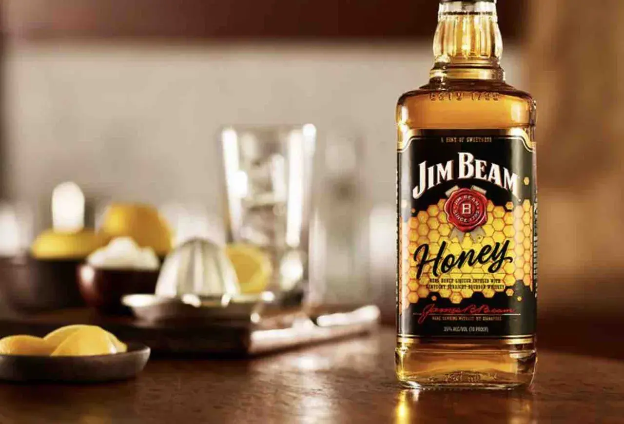 Butelka Jim Beam Honey na drewnianym blacie, obok cytryny i wyciskarki. Idealna na letnie wieczory.