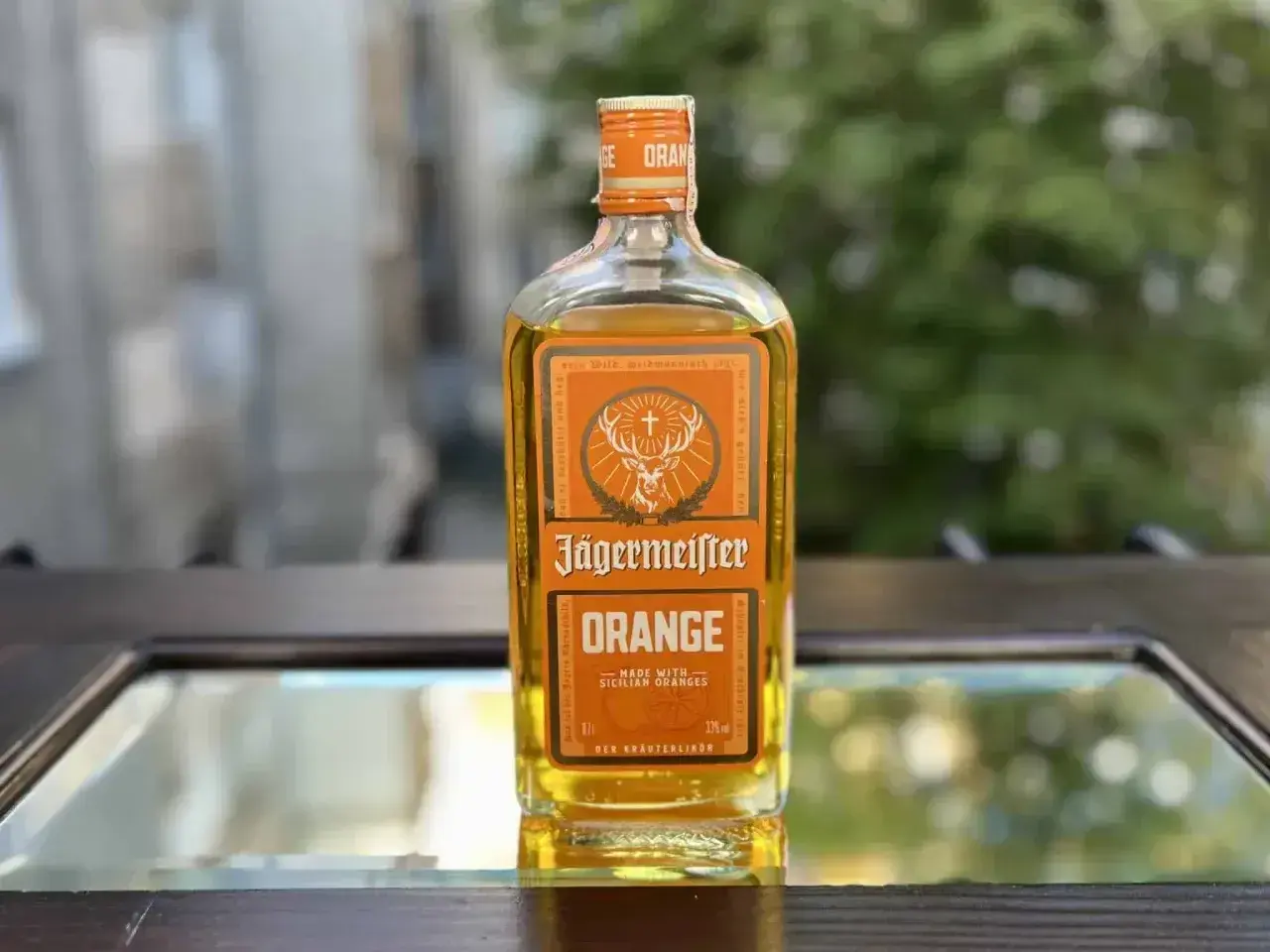 Butelka Jägermeister Orange, z pomarańczowym akcentem, stoi na szklanym blacie.