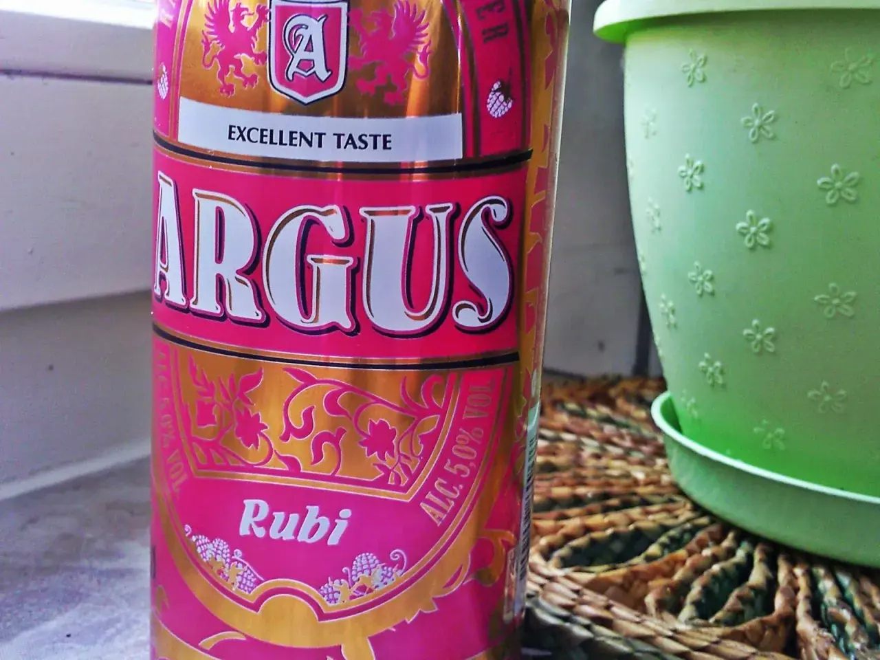 Puszka piwa Argus Rubi z napisem "Excellent Taste", obok zielona doniczka.