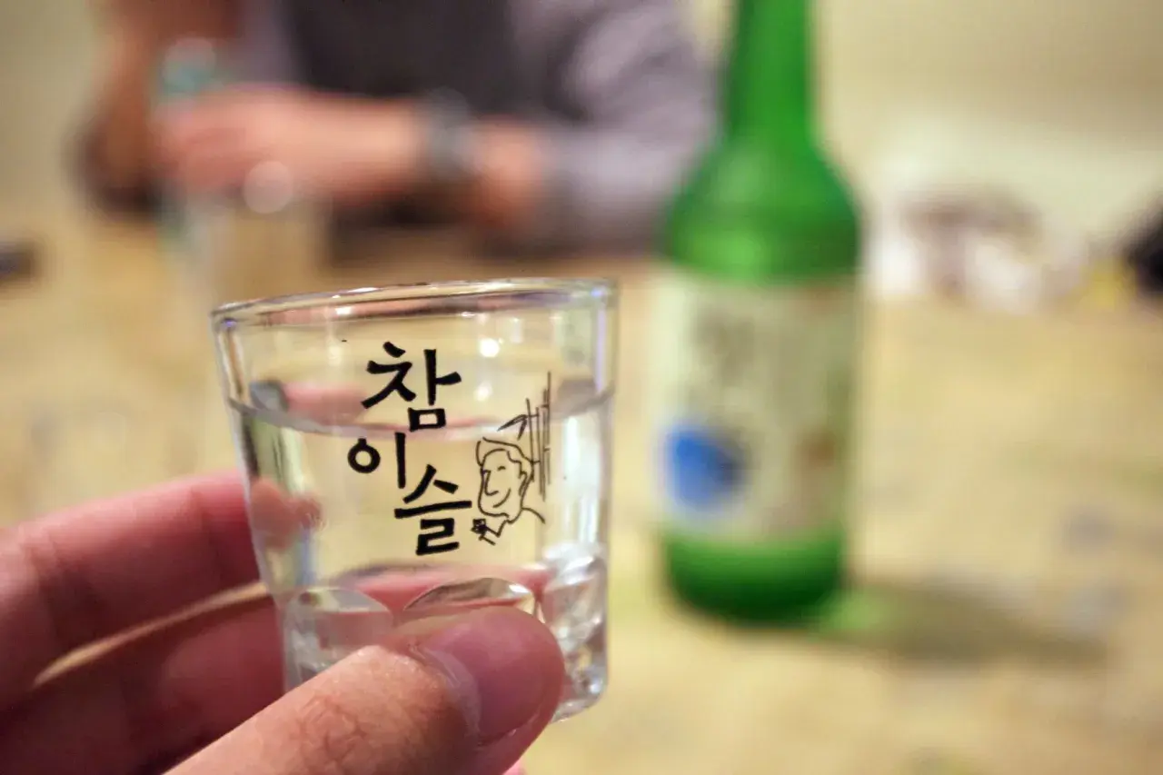 Szklaneczka z soju, na której widnieje napis "참이슬" i rysunek. Zastanawiasz się, soju ile procent?