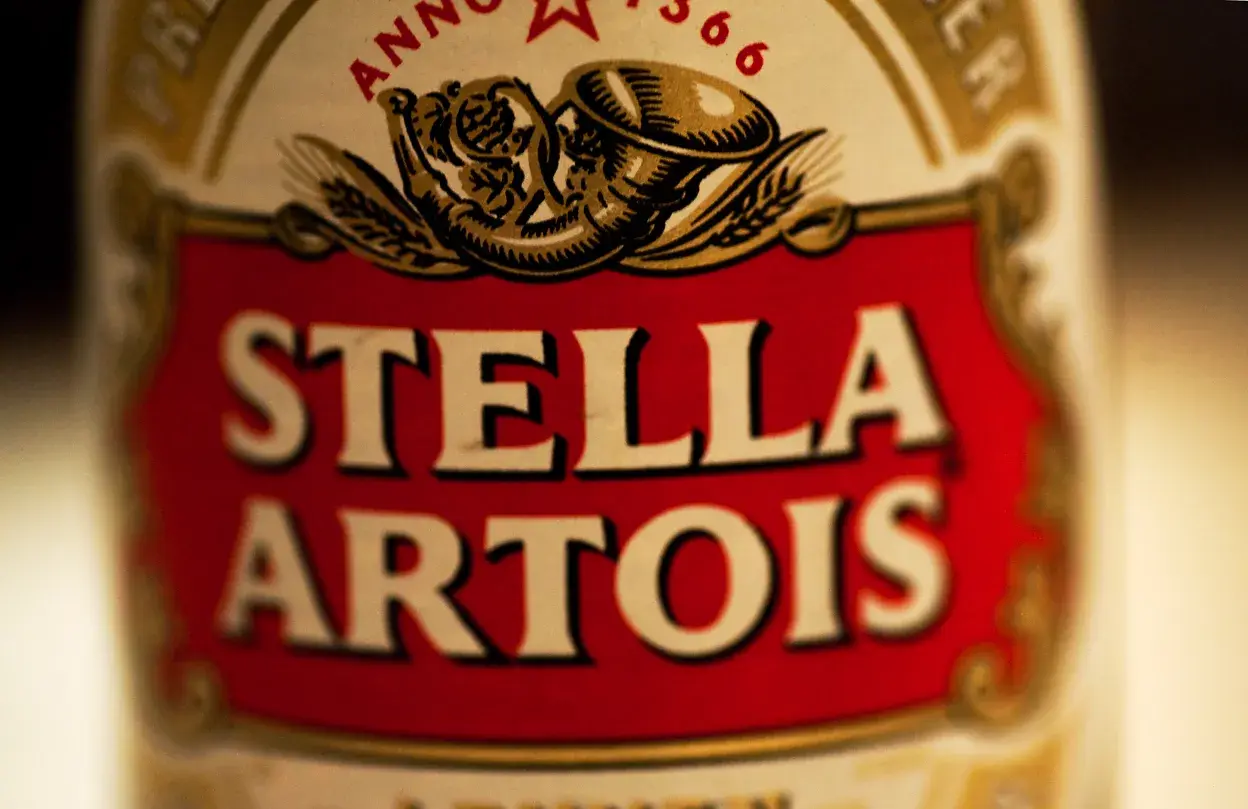 Zbliżenie na etykietę piwa Stella Artois. Czerwone tło z białym napisem.