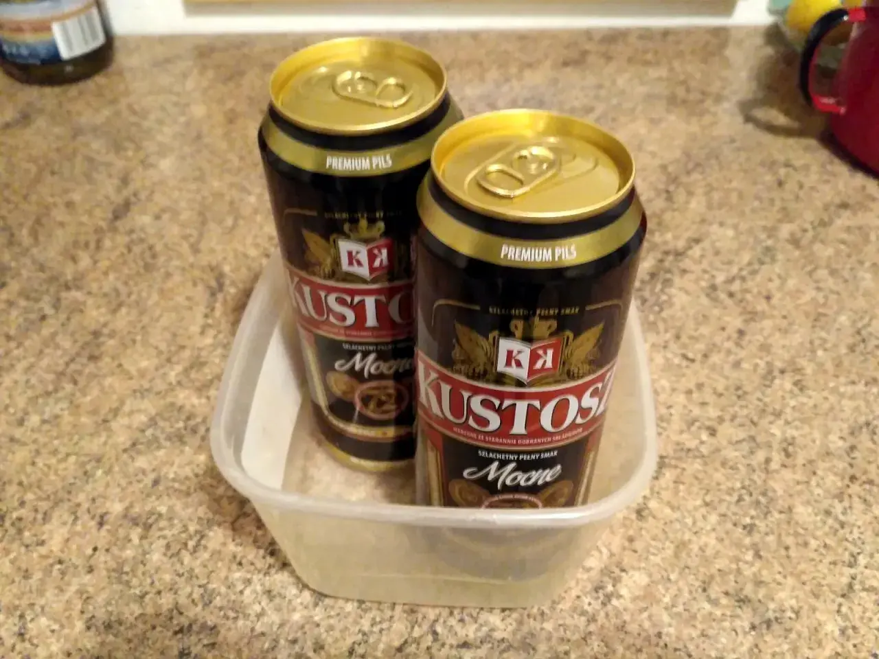 Dwa puszki piwa Kustosz Premium Pils w plastikowym pojemniku. Idealne na wieczór z dobrym **kustosz piwo**.