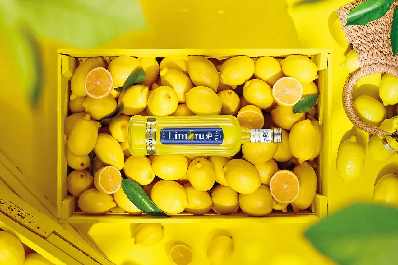 Butelka Limoncé Spritz leżąca w skrzynce pełnej cytryn.