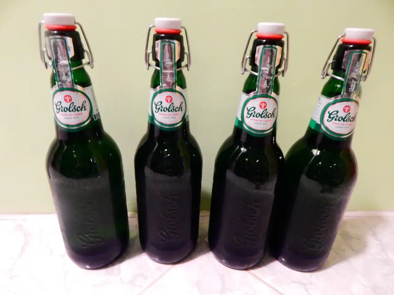 Cztery butelki piwa Grolsch z charakterystycznymi zamknięciami typu swing-top, stojące obok siebie.