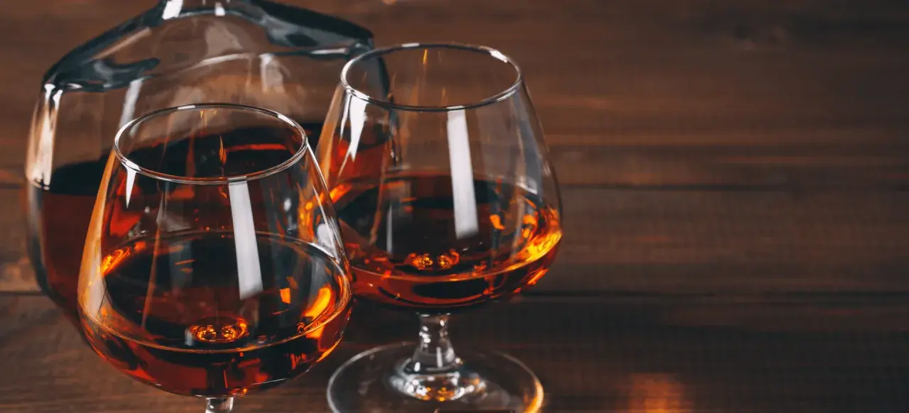 Dwa kieliszki z bursztynowym koniakiem i karafka na drewnianym stole. Idealny wieczór z brandy.