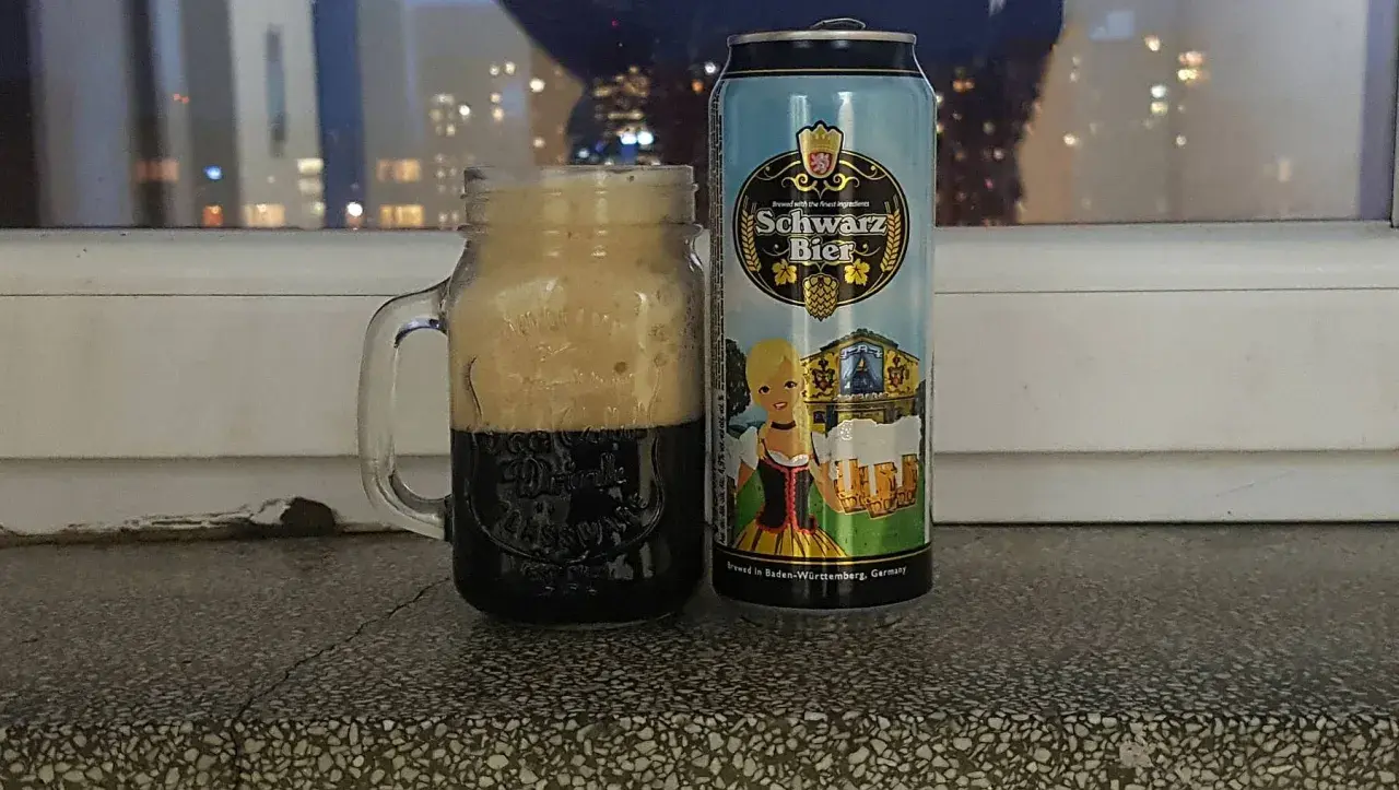 Perlenbacher Schwarz Bier w kuflu, obok puszka piwa. W tle nocne światła miasta.