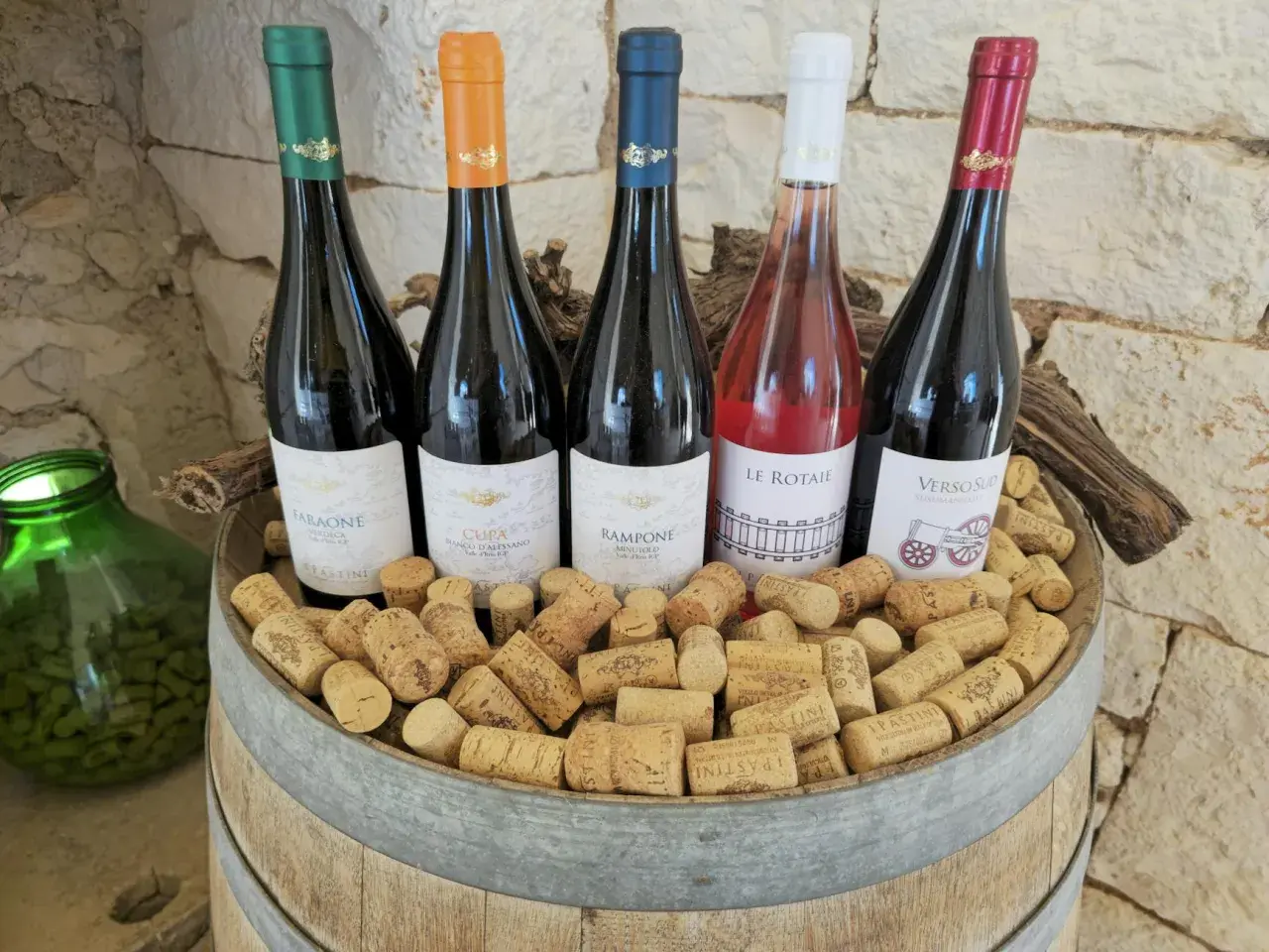 Pięć butelek wina, w tym różowe, na beczce pełnej korków. Idealne na tanie wino i wieczorne degustacje.