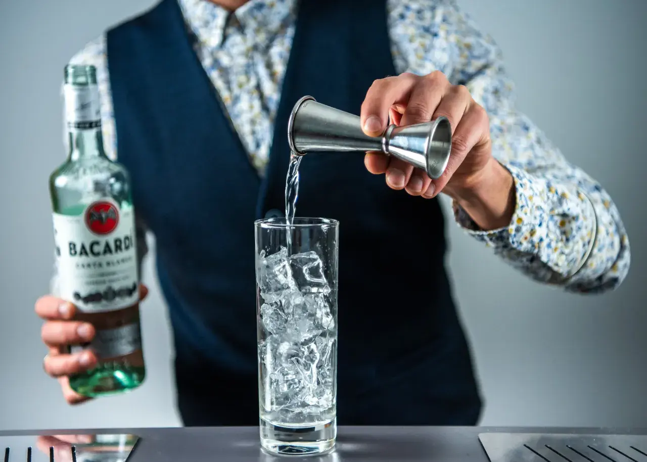 Barman nalewa rum z butelki Bacardi do szklanki z lodem, przygotowując drinka rum z colą.