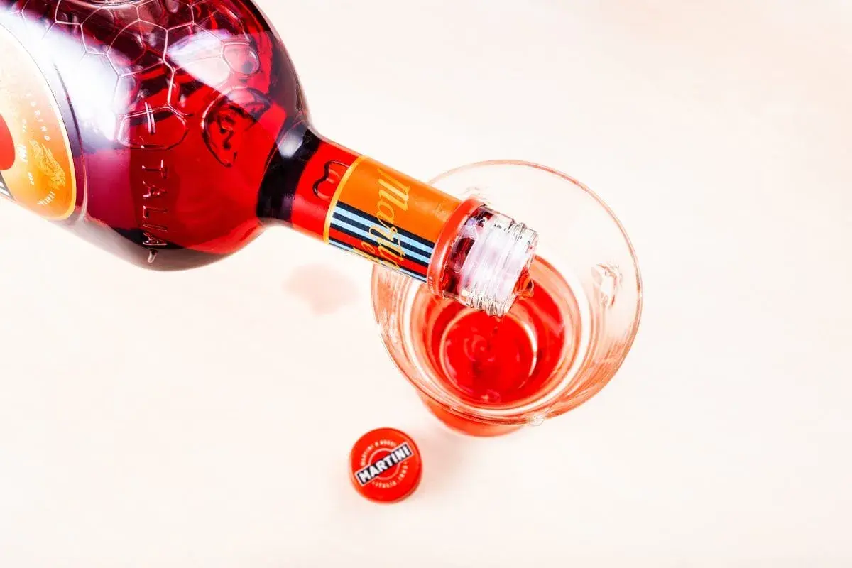 Czerwony Martini Fiero nalewany do kieliszka. Obok leży czerwona zakrętka z logo Martini.