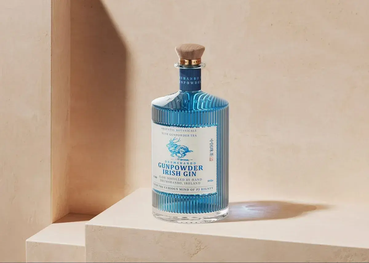 Niebieska butelka ginu Drumshanbo Gunpowder Irish Gin, inspirowanego podróżami do Bombaju, z drewnianym korkiem i etykietą z jeleniem.