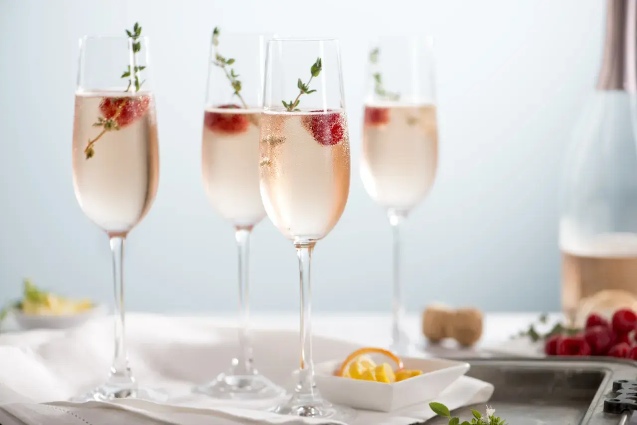 Cztery kieliszki orzeźwiającego prosecco rose z malinami i gałązkami tymianku, gotowe na toast.