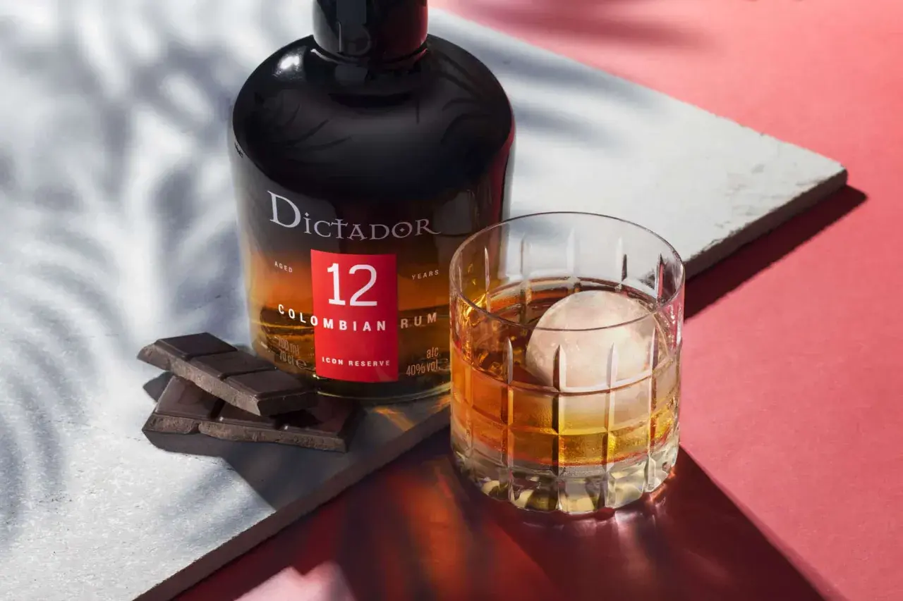 Butelka rumu Dictador 12 Years Colombian Rum obok szklanki z drinkiem i kawałków czekolady.
