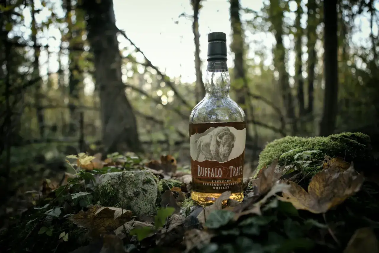 Butelka burbona Buffalo Trace stoi w jesiennym lesie, otoczona liśćmi i mchem.