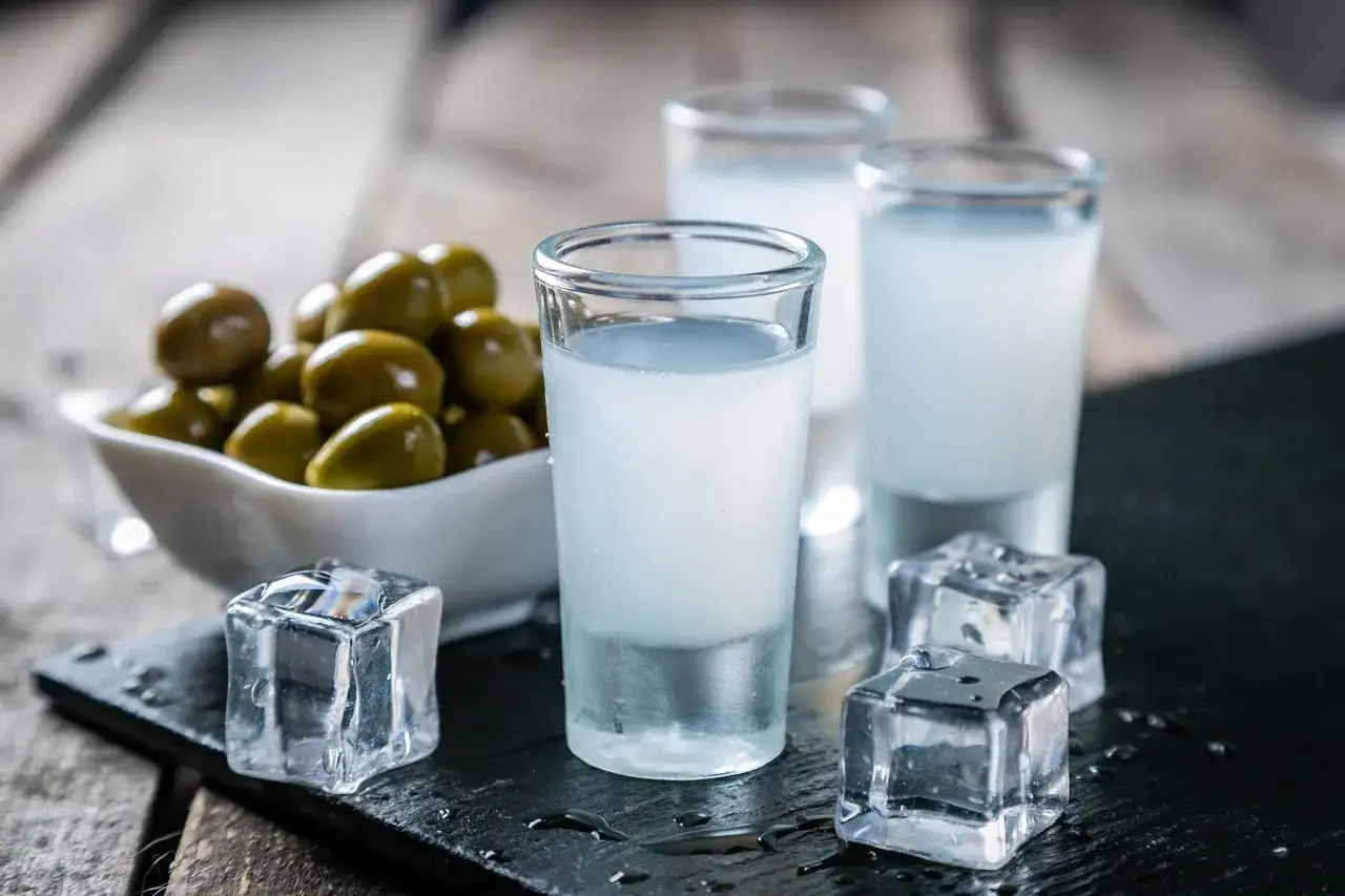 Trzy kieliszki z białym alkoholem, kostki lodu i miseczka oliwek. Idealne na grecki wieczór, jak na Akropolu.
