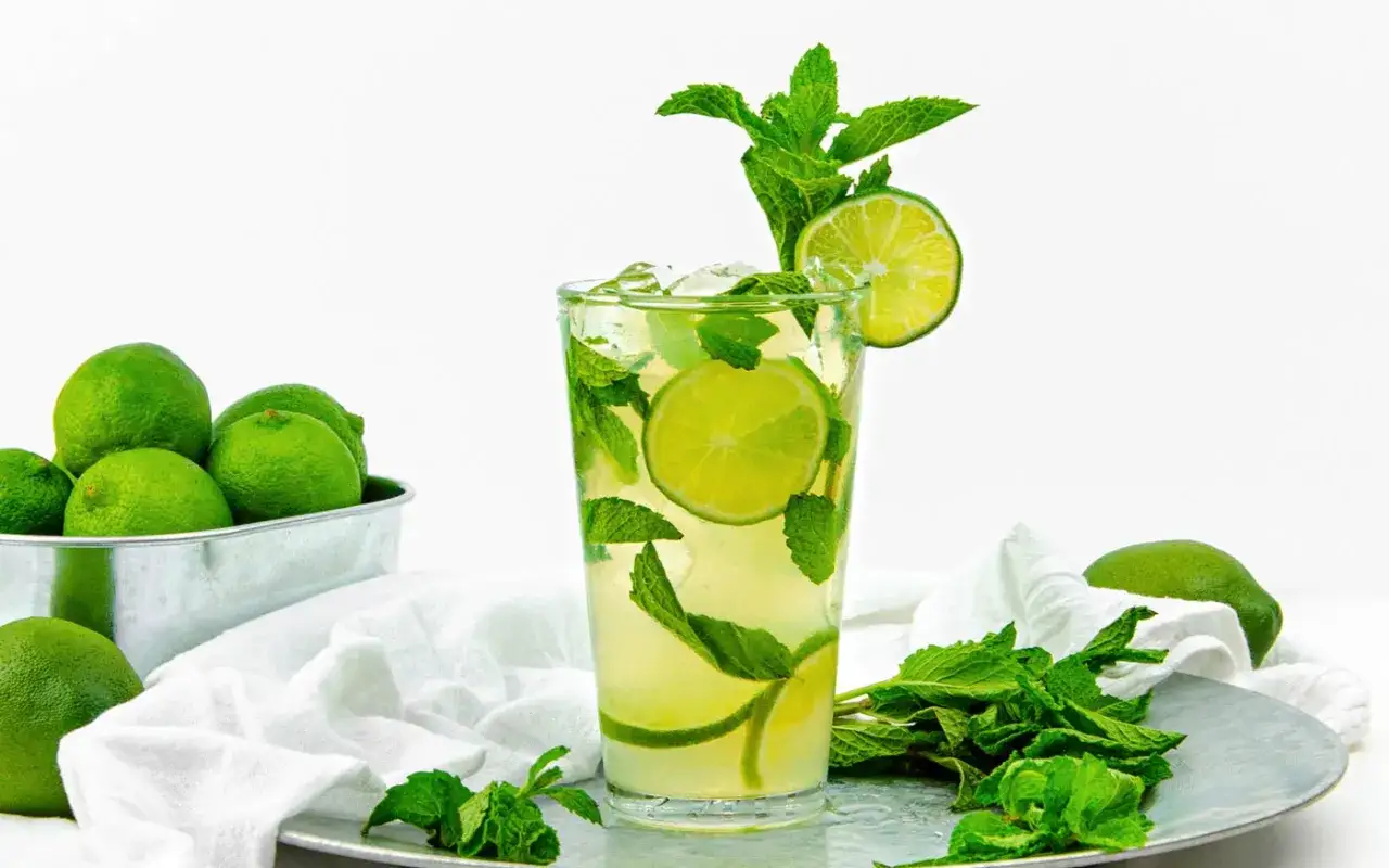 Orzeźwiający mojito z limonką i miętą, otoczony świeżymi owocami i ziołami. Idealny na upalne dni.