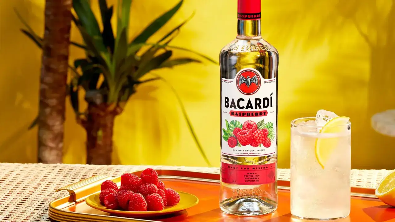 Butelka Bacardi malinowe obok talerzyka z malinami i drinka z lodem i cytryną. Idealne na letnie wieczory.