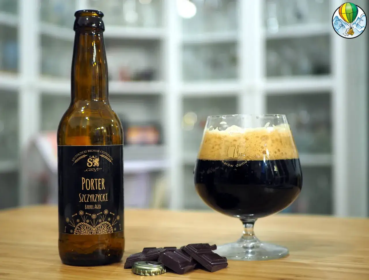 Butelka i kielich z ciemnym, mocnym piwem typu porter, obok kawałki gorzkiej czekolady i kapsel.