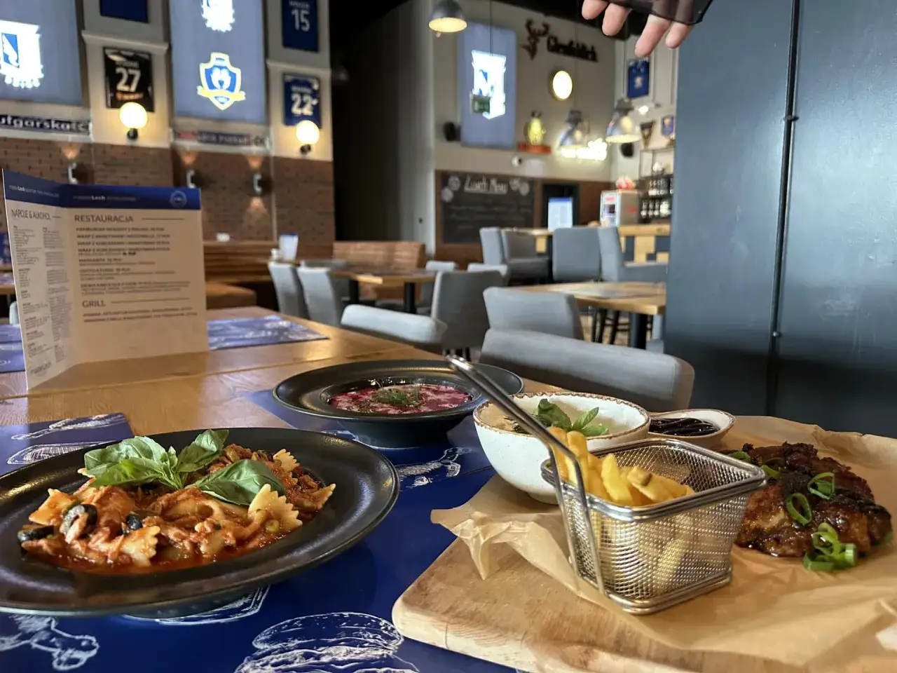 Pyszne dania w restauracji Lech, w tym makaron farfalle, zupa i frytki. W tle koszulki klubowe.