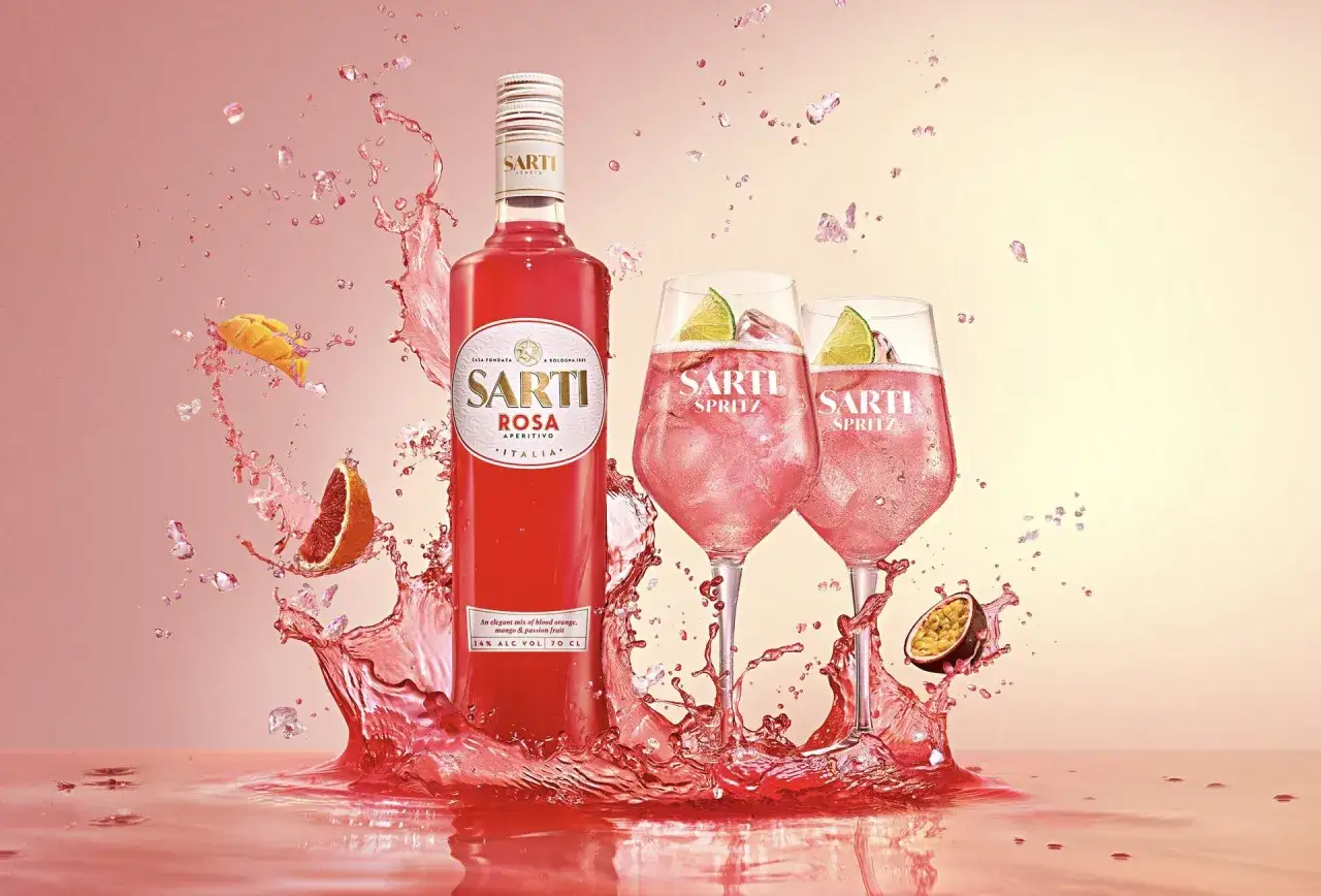 Sarti Rosa Aperitivo w towarzystwie dwóch kieliszków Sarti Spritz, otoczonych dynamicznymi rozbryzgami różowego płynu i owoców.