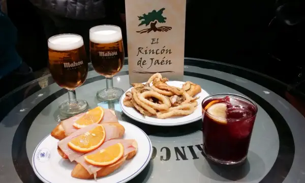 Dwa piwa Mahou, tapas z szynką i pomarańczą, smażone kalmary i sangria na stole w El Rincón de Jaén.