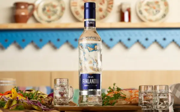 Butelka wódki Finlandia z kieliszkami i przekąskami na stole.