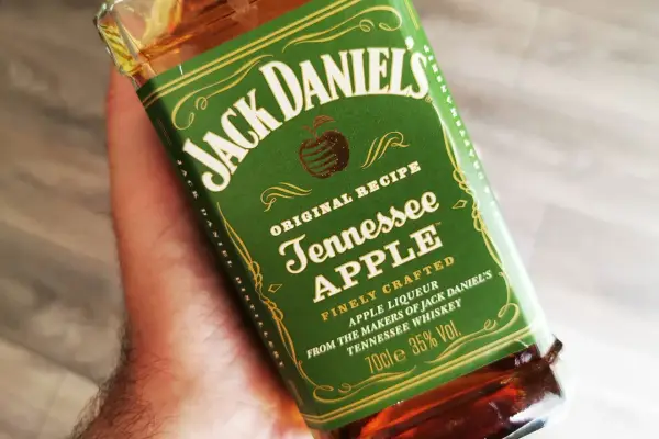 Dłoń trzyma butelkę Jack Daniel's Tennessee Apple. Ten miodowy likier jabłkowy to idealny dodatek do wieczoru.